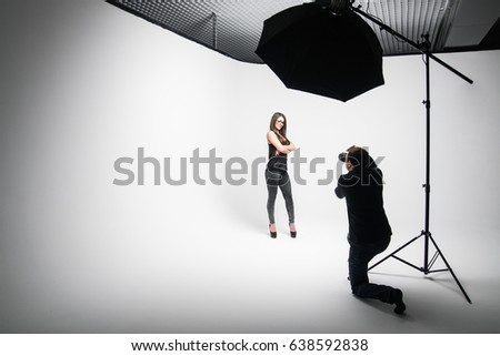 Girl the photographer takes pictures of model in black on a white background in Studio