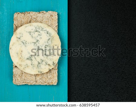 Blue Stilton Cheese on Thin Crisp Wholewheat Crackers Against a BLue and Black Background