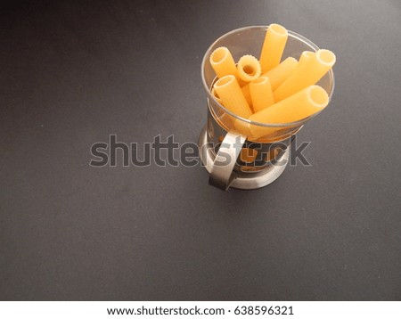 Macaroni Pasta tubes in glass that is inside a silver tea glass holder. On black background to top right of picture. Macro shot.