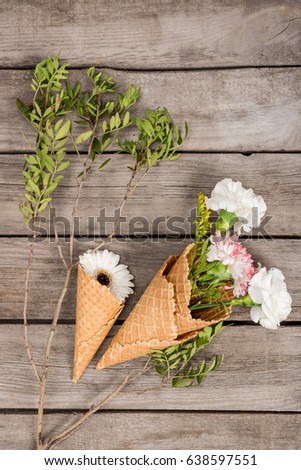top view of flowers in sugar cones laying on wooden table, wooden background