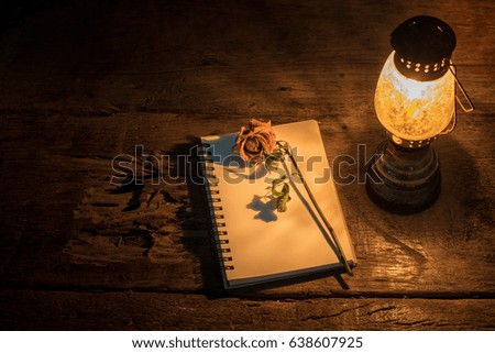 Kerosene lamp with dried rose and letter on wicker mat and wooden planks background