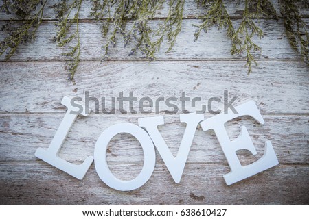 White LOVE  character on old wooden background with dry flowers around