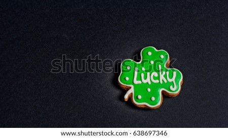 Clover ginger cookie on black background for St. Patrick's day with inscription Lucky.