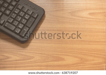 The old black keyboard is on a scratched brown desk, a computer device that is used to input data with wooden background.