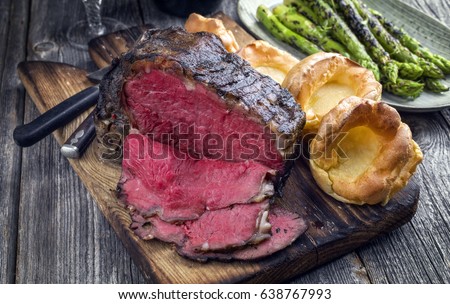 Barbecue dry aged Rib of Beef with green Asparagus and Yorkshire Pudding as close-up on an old cutting board