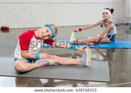 Adorable little girls in sportswear exercising on yoga mats in gym, children sport school concept