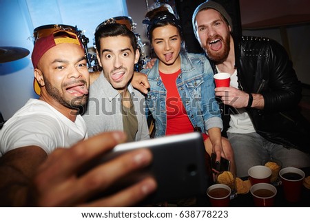 Group of modern young people chilling at night club party, posing for selfie photo, grimacing and having fun
