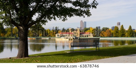 Denver city skyline with view of city park lake and bench. Critical focus on bench and silhouetted tree at left.