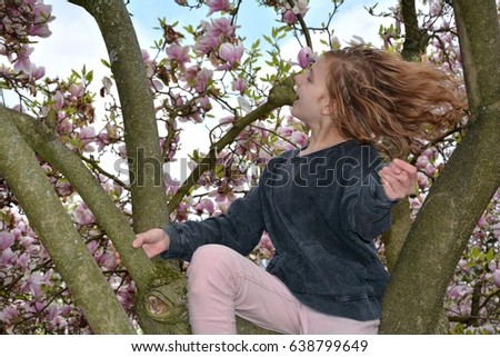 A girl sits in a magnolia tree and shakes the head and lets the hair fly 
