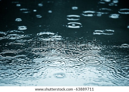 Rain drops rippling in a puddle with blue sky reflection Royalty-Free Stock Photo #63889711