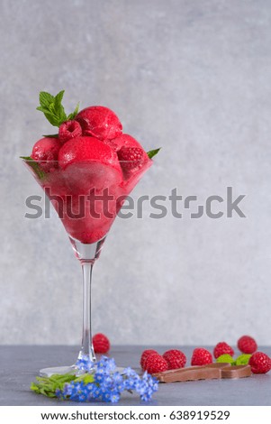 Raspberry ice cream sorbet in high glass with chocolate spoon, raspberry, mint leaves and blue flowers, copy space