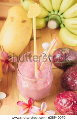 Tropical fresh smoothie in a glass. Strawberry shake on light wooden table. Bananas, Dragon, passion fruit and frangipani flowers on background