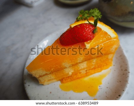 A single piece of orange cake with orange syrup on a white plate decorated with a piece of strawberry on a white marble table.