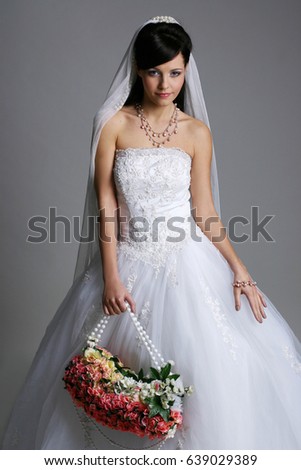 Studio portrait of a bride young woman in a white dress and veil with color flowers woman bag
