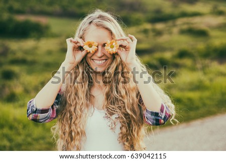 Portrait of beautiful blonde woman covering eyes with flowers at the country road.Leisure time at the countryside
Image is intentionally toned.
