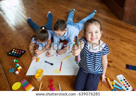 
Children draw on paper and play on a brown wooden floor