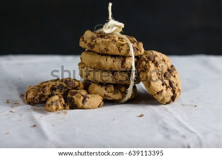 Stack of four chocolate chip cookies bound with straw twine on white tablecloth and black background
