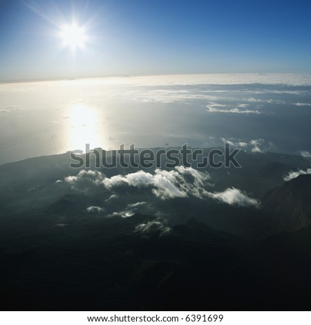 Aerial view of mountainous terrain in Maui, Hawaii with sun shining off the Pacific ocean in background.