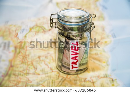 Travel budget - vacation money savings in a glass jar on world map. Collecting money for travel. Glass tin as moneybox with cash savings (banknotes and coins) on table and map as background.