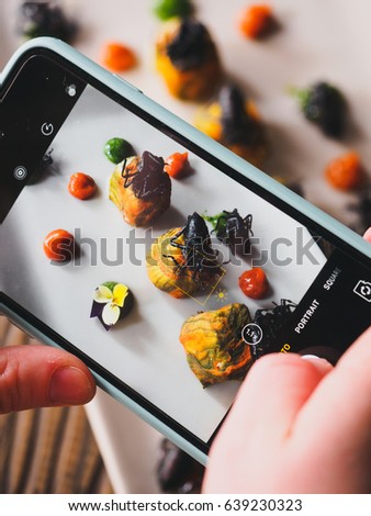 Soft cheese in zucchini flowers with beetles on a wooden table. Mesoamerican cuisine in a Mexican Restaurant, Mexico City. Girl taking pictures of weird food with smartphone. Vertical photo