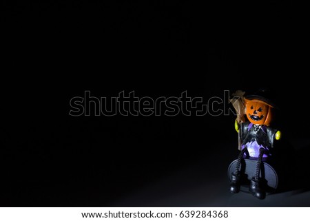 Witch Pumpkin Ghost Doll Sitting on Artificial Grass at Darkness Night. Copy Space for Text. Idea Concept for Halloween Background.