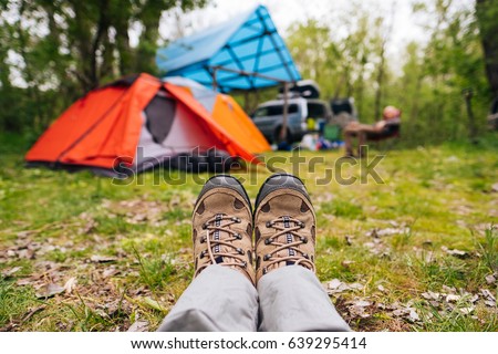 Traveler hiking boots near camping tent outdoors. Trekking shoes on nature campsite in the forest. Travel healthy active lifestyle freedom background. Feet selfie. Woman relaxing after hiking. Royalty-Free Stock Photo #639295414