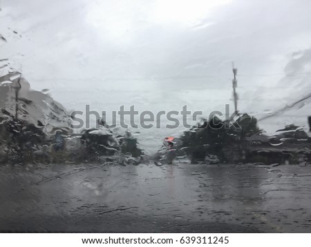 Abstract background of raindrop on transparent glass in front of a car showing rainy sky covering over road in town