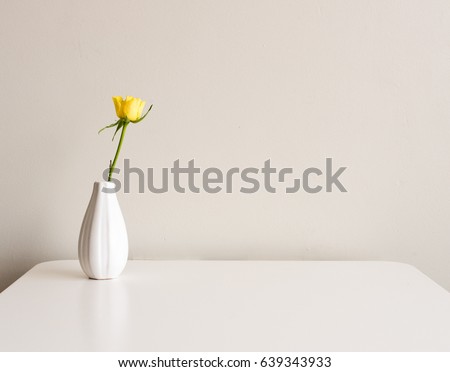 Yellow rose in small white vase on white table against neutral background