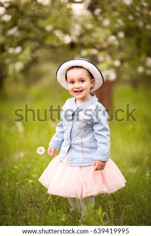 Little girl in a hat with a dandelion on a walk in a spring park or garden