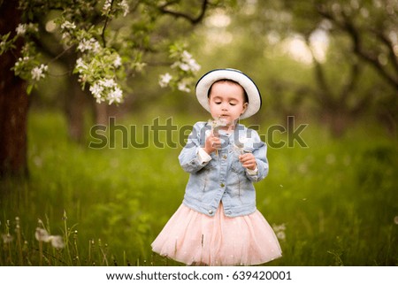 Little girl in a hat with a dandelion on a walk in a spring park or garden