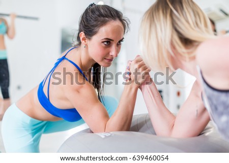Front view of strong muscular young woman arm wrestling on Swiss ball with a female opponent looking in her eyes in sports center