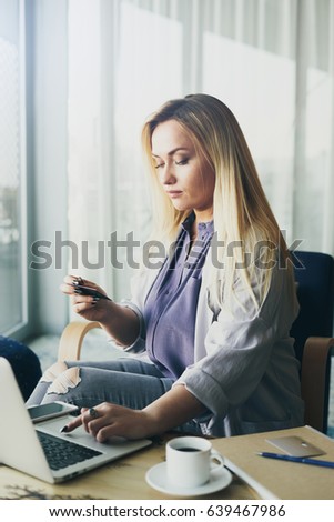 Professional business woman is booking flight tickets online by using portable computer while sitting in a coffee shop. Entrepreneur female is looking at a visiting card while searching email address 