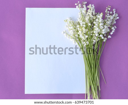 Spring lily flowers and paper card on violet vintage background from above in flat lay style. Greeting for Women or Mothers Day.