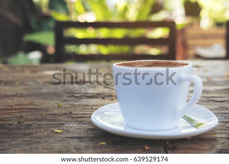 A white cup of hot coffee on vintage wooden table with blur green nature background 