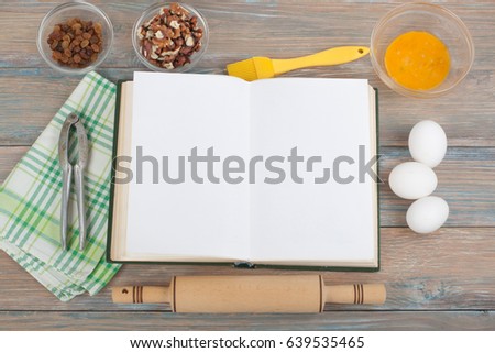 Open recipe book on wooden background, wooden spoon, rolling pin , checkered tablecloth