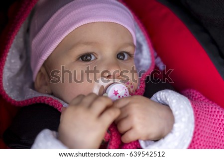 Beautiful 1 year old baby in a stroller attached in a car seat. Outdoors in cold weather
