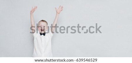 Happy cheerful kid with hands up against the grey wall