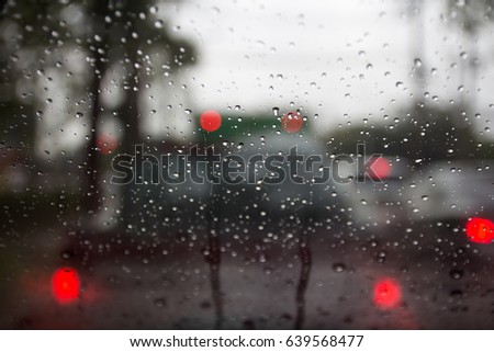 blury car stopped on traffic lights waiting for go on in rainy day with bokeh on windshield