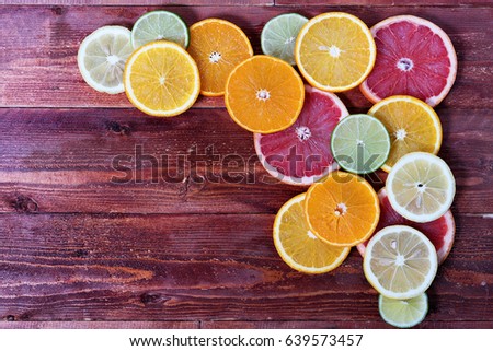 round slices of different citrus fruits stacked in a corner on a red wooden background