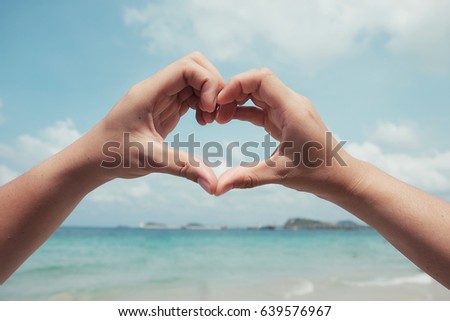 Couple hands showing heart shape with sky background at the beach, love concept.