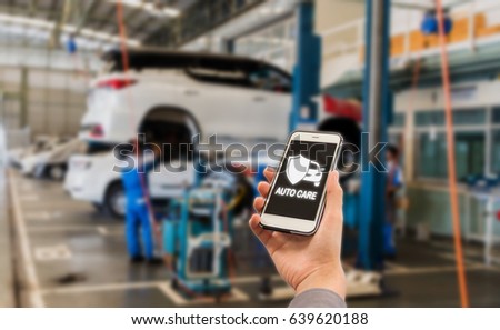 auto care application on smartphone with Blurred picture of car garage with cars being under maintenance and technicians for background