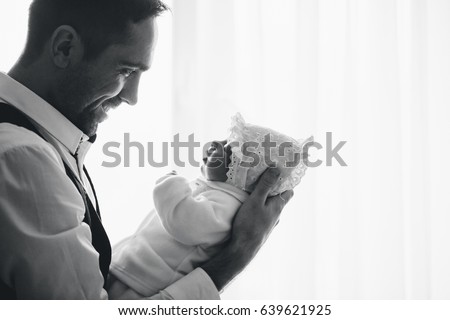 Happy loving handsome father holds his small newborn daughter. Profile backlit black and white picture.