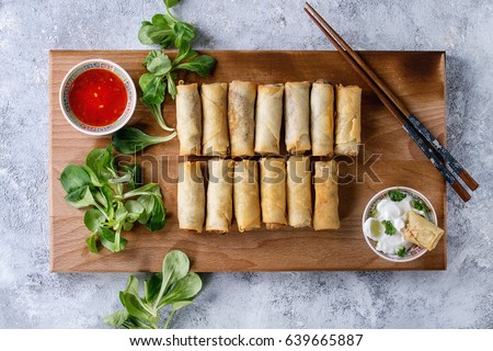 Fried spring rolls with red and white sauces, served on wood serving board with fresh green salad and wooden chopsticks over gray blue texture background. Flat lay, space. Asian food Royalty-Free Stock Photo #639665887