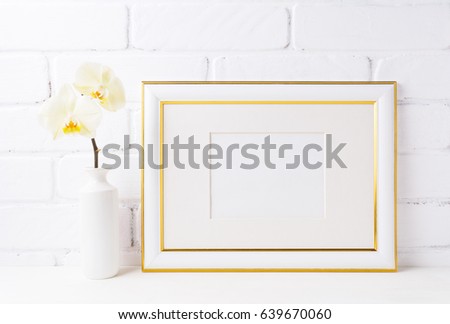 Gold decorated landscape frame mockup with soft yellow orchid in vase. Empty frame mock up for presentation artwork. Template framing for modern art.