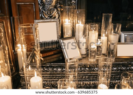 Frames with clear papers stand on bunches of books between candles on fireplace