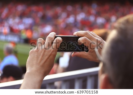Selective focus on hands using mobile phone taking picture of sport match