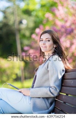 Young woman in the park listening to music on headphones in the spring