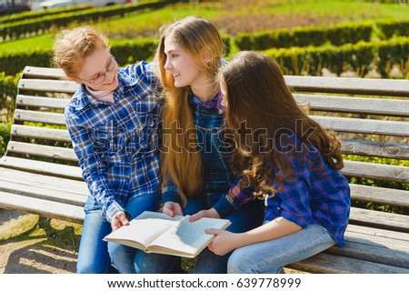 Little pretty schoolgirls reading a book and sitting on bench outdoor