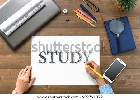 Girl draw text STUDY on paper sheet at the table with a mobile phone, a laptop, business accessories