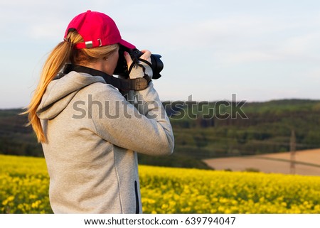 Young tourist woman photographing landscape with rape field. Woman taking pictures of the countryside.